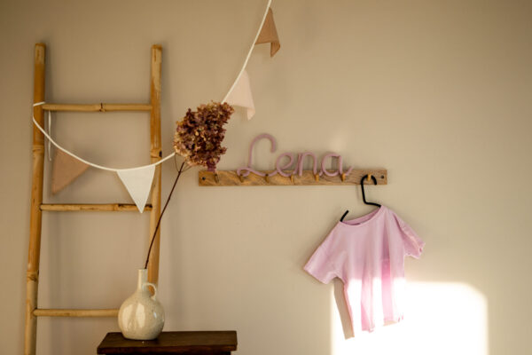 Imię ze sznurka Lena stoi na drewnianym wieszaku ściennym w pokoju dziecka.