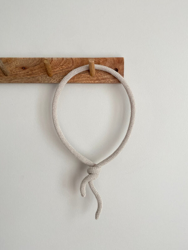 Dekoracja ze sznurka w kształcie balonika wisi na drewnianym wieszaku ściennym.