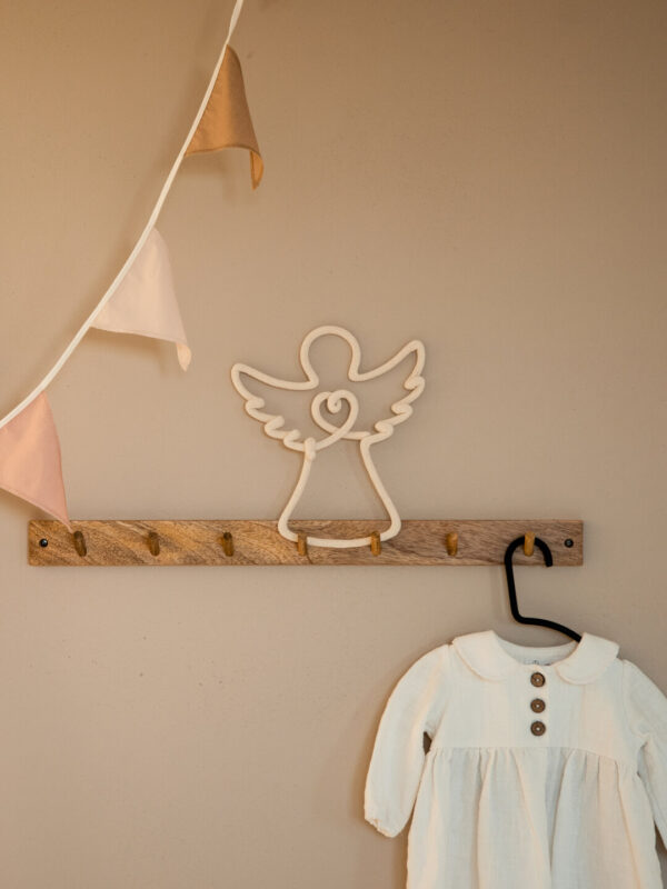 Aniołek ze sznurka znajduje się na drewnianym wieszaku w pokoju dziecka.