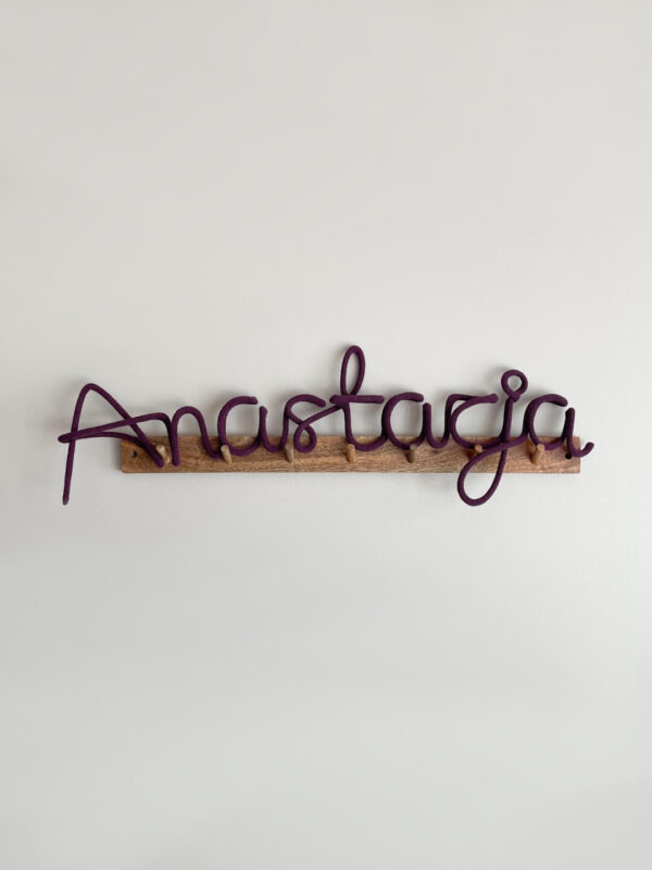 Imię ze sznurka Anatazja wisi na ścianie na drewnianym wieszaku.
