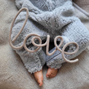 Napis ze sznurka o treści love leży na nóżkach niemowlaka.