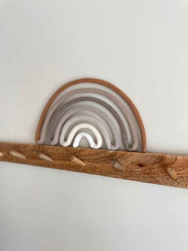 Tęcza ze sznurka w kolorach beżu stoi na wieszaku z drewna przymocowanym do ściany.