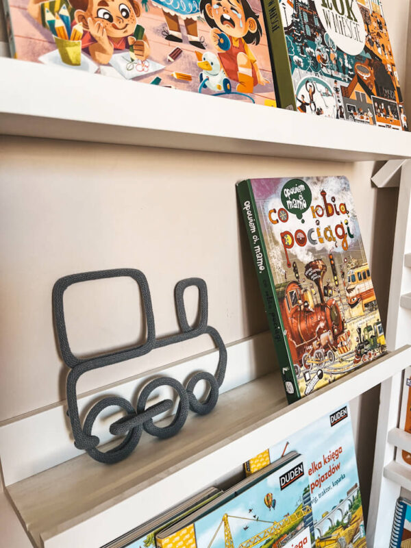 Dekoracja ze sznurka w kształcie pociągu stoi na półce z książkami dla dzieci.