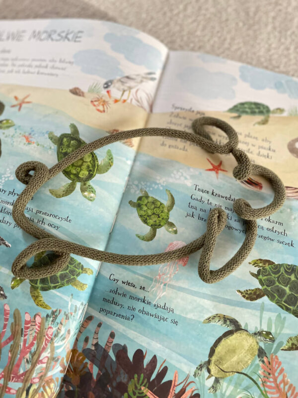 Ozdoba ze sznurka w kształcie żółwia leży na otwartej książce na stronach przedstawiających żółwie morskie.