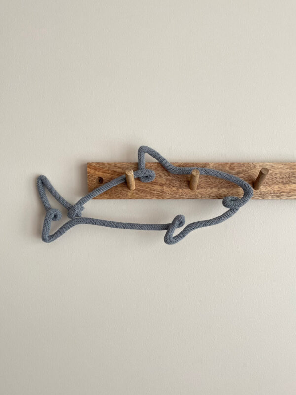 Dekoracja dziecięca w kształcie rekina wisi na drewnianym wieszaku ściennym.