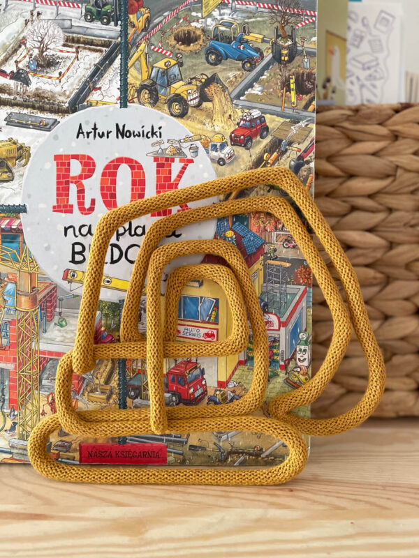 Dekoracja dziecięca ze sznurka w kształcie koparki stoi oparta o książkę pod tytułem Rok na placu budowy.