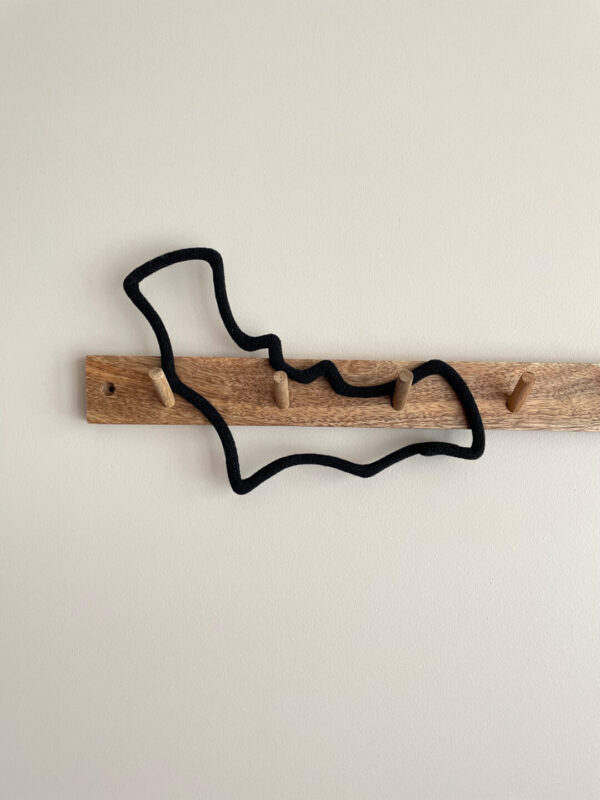 Dekoracja ze sznurka w kształcie nietoperza wisi na drewnianym wieszaku ściennym.