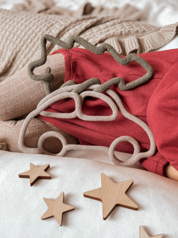 Świąteczna ozdoba z drutu i sznurka w kształcie auta z choinką stoi oparta o śpiącą dziewczynkę, a przed nią leżą gwiazdki ze sklejki.